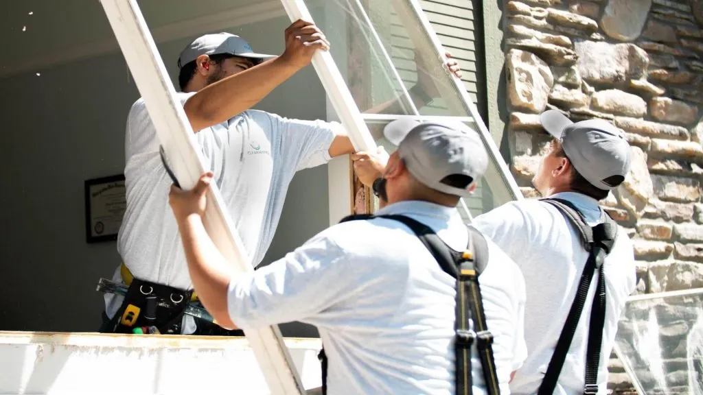 Three Clearwater workers lift a replacement window into a window frame